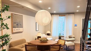 A modern living room with a round wooden dining table, two armchairs, a sofa, and a hanging light fixture. - River Place -Walk to Jefferson Methodist, 2BR Queen Beds 1 Bath -Patio & Grill (Philadelphia)