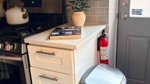 A kitchen with a stove, oven, white cabinets, a potted plant, a book, and a trash can. - River Place -Walk to Jefferson Methodist, 2BR Queen Beds 1 Bath -Patio & Grill (Philadelphia)