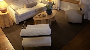 A cozy living room with a sofa, armchair, ottoman, and a small table with a lamp and a plant. - River Place -Walk to Jefferson Methodist, 2BR Queen Beds 1 Bath -Patio & Grill (Philadelphia)
