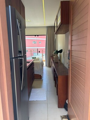 A narrow hallway with a kitchenette on one side, a dining area with a table and chairs, and a view of a building outside. - Mar Dá Liberdade com Amerigo Vespucci (Cairu)