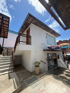 A two-story building with a staircase leading to the upper floor, a potted plant, and a covered entrance area. - Mar Dá Liberdade com Amerigo Vespucci (Cairu)