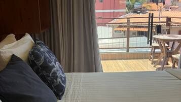 A hotel room with a bed, a wooden wardrobe, a view of the cityscape, and a balcony with a table and chairs.