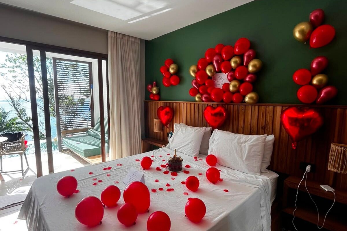 A hotel room with a bed, a view of the outdoors, and a green wall with heart-shaped decorations.
