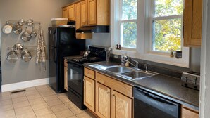 Une cuisine moderne avec des meubles en bois, un réfrigérateur noir, des appareils électroménagers en acier inoxydable et une fenêtre donnant sur des arbres.