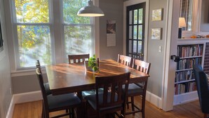 Une salle à manger avec une table en bois, six chaises, une plante en pot et un luminaire suspendu.