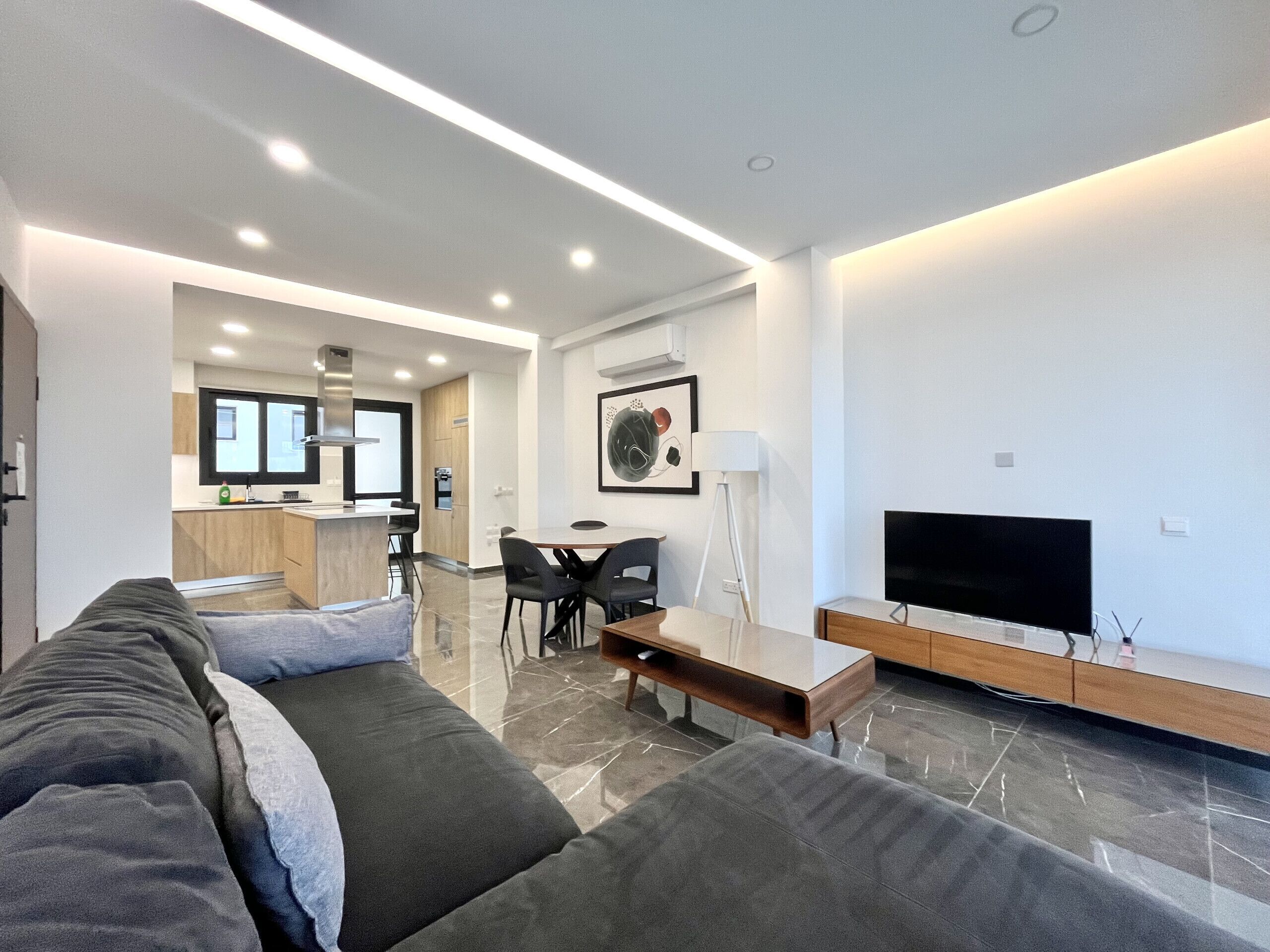 Een moderne woonkamer met een bank, een televisie en een eethoek met stoelen en een tafel.