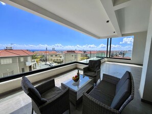 A balcony with wicker furniture, a glass table, and a view of buildings and the sea. - STAY Anna Residence Sea View Apartment 201 (Agios Athanasios)