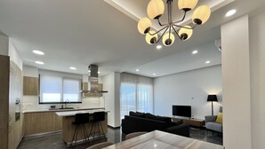 Et moderne køkken med en central ø, et spiseområde med et stort træbord og en stue med sofa og fjernsyn.
