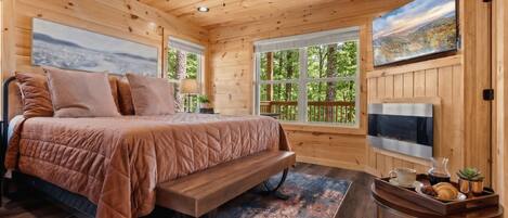 A wooden cabin bedroom with a bed, ceiling fan, large windows, and a TV.
