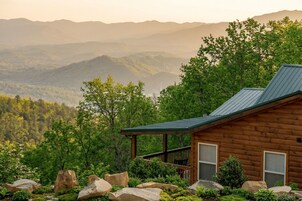 Eine Hütte mit Veranda, umgeben von großen Steinen und Pflanzen, mit Blick auf eine Berglandschaft.