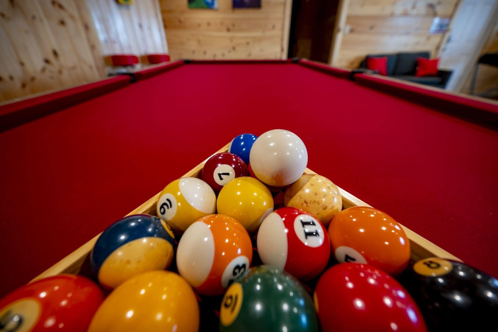 A pool table with a red felt surface and a wooden border, surrounded by various numbered billiard balls.