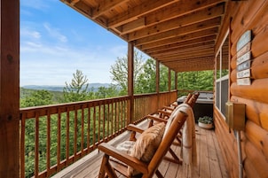 Eine Holzdachterrasse mit Bergblick, eine Holzbank mit Kissen und ein Schild mit Wegweisern.