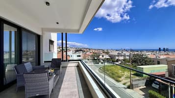 Ein Balkon mit Korbmöbeln, einer Glastrennwand und Blick auf die Stadt.