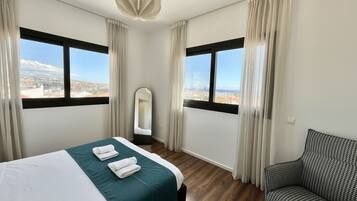 Ein Hotelzimmer mit Bett, Stuhl, Spiegel und großen Fenstern mit Blick auf die Stadt.