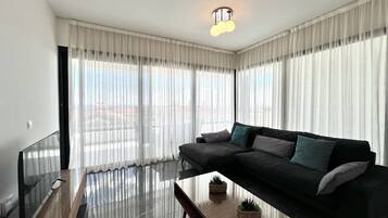 Ein modernes Wohnzimmer mit einem schwarzen Sofa, einem Glastisch und transparenten Vorhängen.