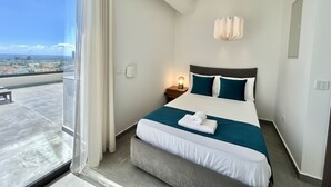 Una habitación de hotel con cama, mesita de noche, lámpara y vista a la ciudad.