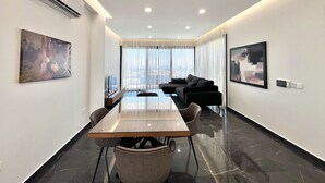 Una habitación de hotel moderna con zona de comedor, sofá y un ventanal con cortinas.