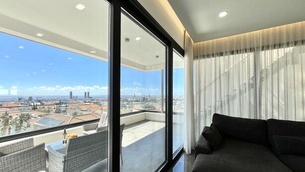 Una sala de estar moderna con un ventanal amplio, un sofá y vistas a un paisaje urbano.