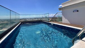 Una piscina en la azotea con barandillas de cristal, vistas a la ciudad y un pequeño cartel en la pared.