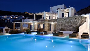 Un área de piscina moderna con muros de piedra, un pérgola y mobiliario exterior.