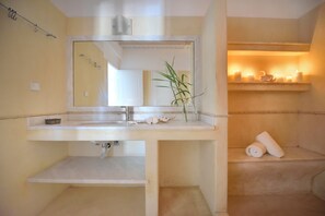 Un bagno con lavandino, specchio, portasciuga asciugamani ed uno scaffale con candele.