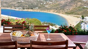 Una mesa de madera con una cesta de frutas y una copa de martini, con vistas a un paisaje costero con casas.