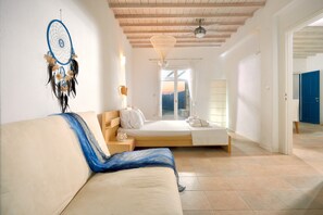 Una camera da letto con un letto, una finestra con tende, una ventola a soffitto e un portafortuna appeso al muro.