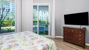 A bedroom with a bed, a dresser, a TV, and a sliding glass door to a balcony. - The Palms of Destin 1111 by Compass Resorts (Destin)
