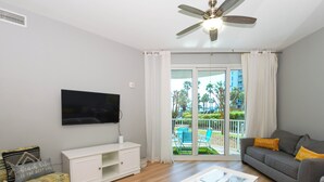 A living room with a flat-screen TV, a ceiling fan, a sofa with cushions, a white console table, and a glass coffee table. - The Palms of Destin 1111 by Compass Resorts (Destin)