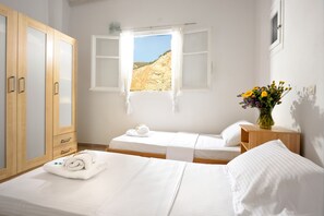 Ett hotellrum med två sängar, en garderob i trä, ett fönster med utsikt över ett bergigt landskap och en vas med blommor på ett nattduksbord.