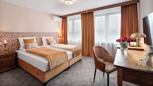 Een hotelkamer met een tweepersoonsbed, een bureau met stoel, een televisie en een vaas met bloemen.