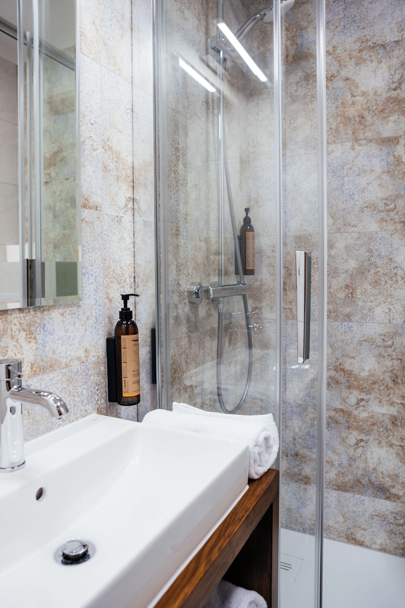 A bathroom with a glass-enclosed shower, a white sink, and a mirror.