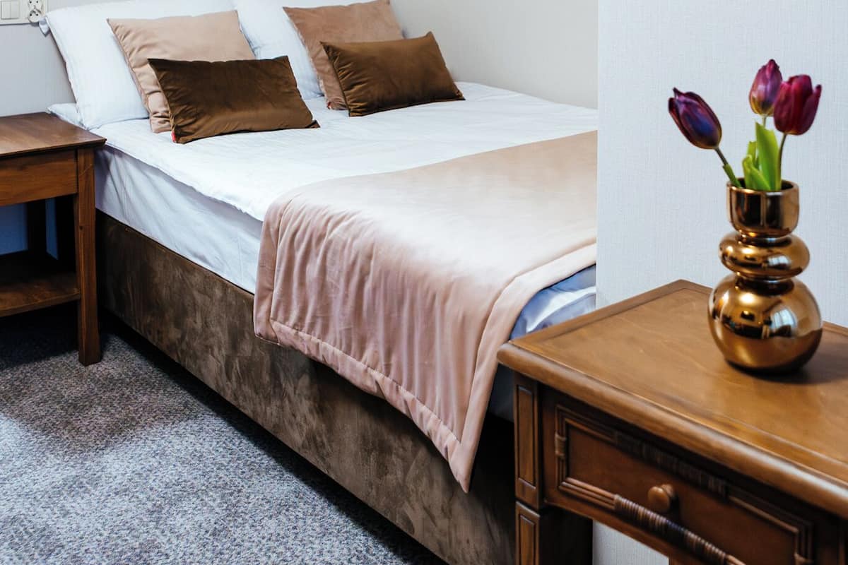 A bedroom with a bed, a bedside table, a nightstand, a dresser, and a vase with flowers.
