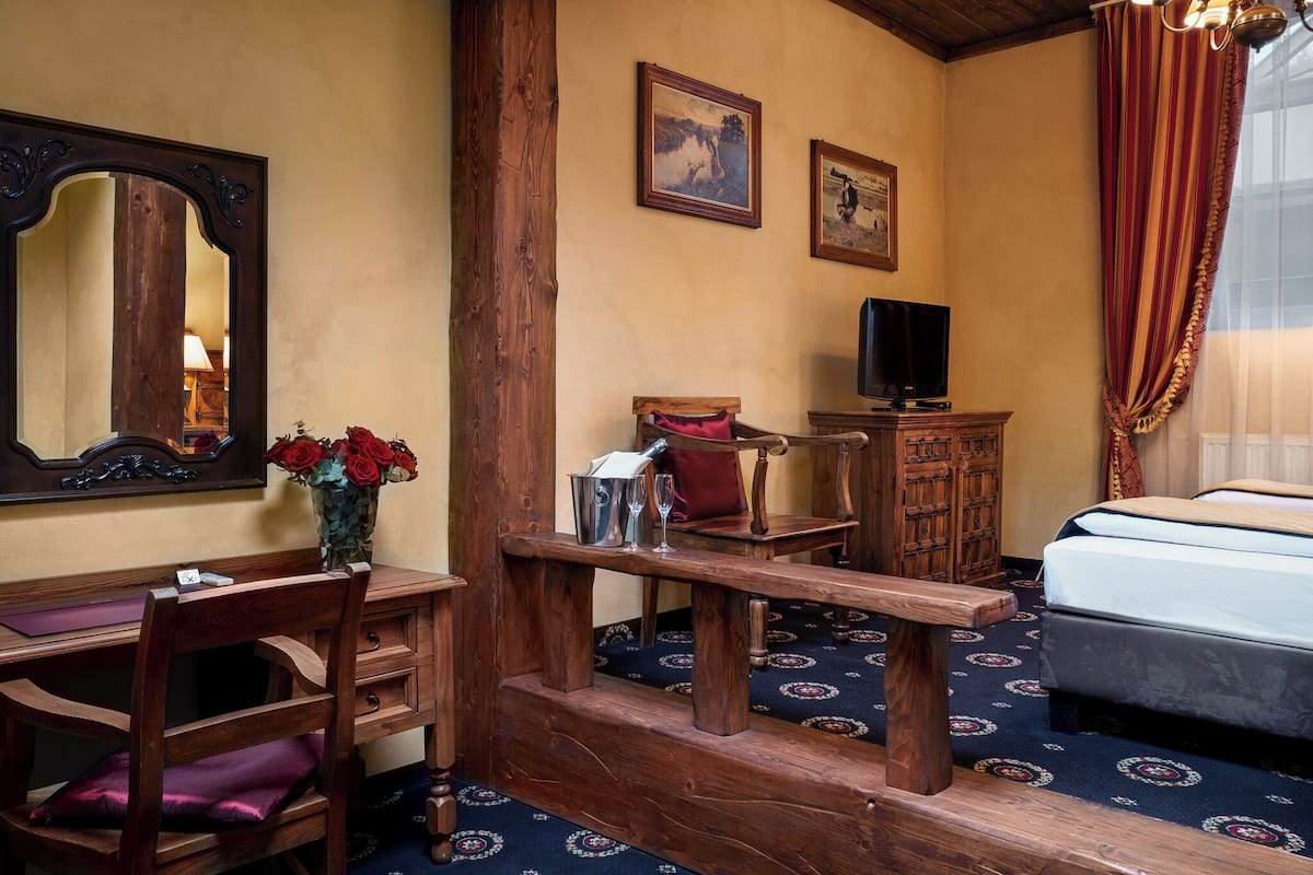 A room with a wooden desk, a chair, a bed, a television, and a mirror.