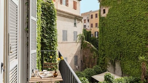 A narrow alleyway with buildings covered in ivy, a wooden table with a vase of flowers, and a balcony with a railing. - Casa Luce, a Burghesius home (Roma)