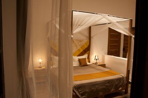 A four-poster bed with a canopy, a bedside table with a lamp, and a wooden headboard.