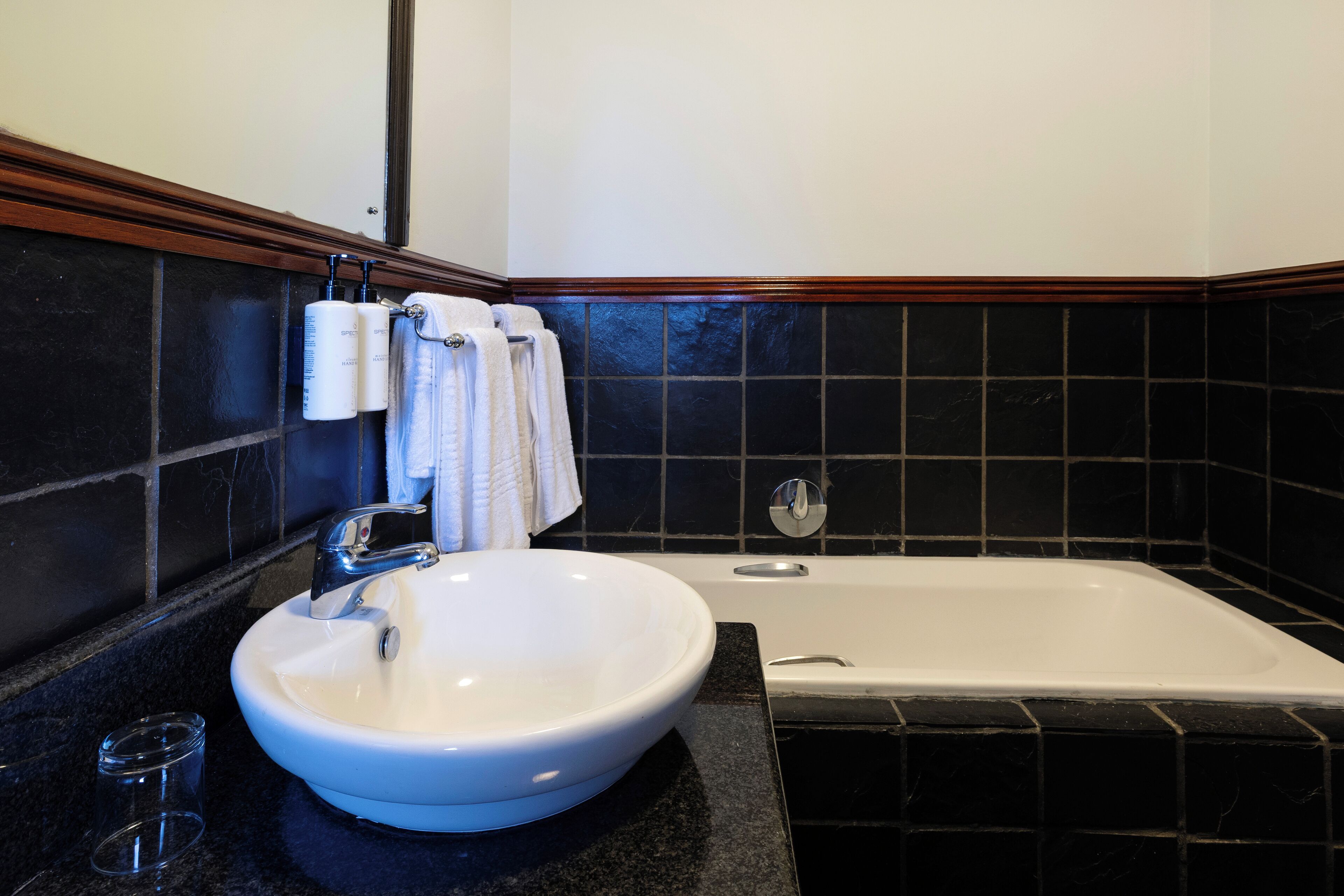 Une salle de bain avec un lavabo blanc, une baignoire et des murs recouverts de carreaux noirs.