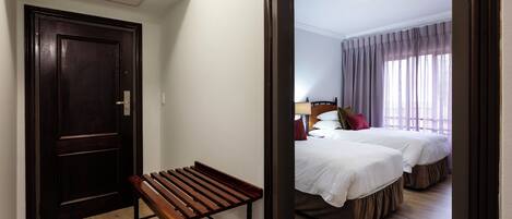 A hotel room with a wooden bench, a double bed, and a large mirror reflecting the room.