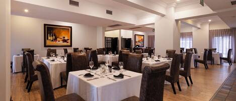 A restaurant with multiple tables and chairs, white tablecloths, and framed artwork on the walls.