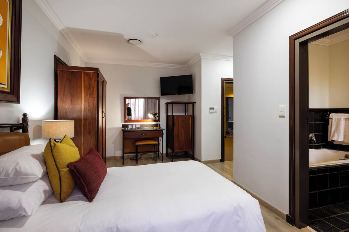 A hotel room with a bed, a desk, a chair, a television, and a bathroom with a bathtub.