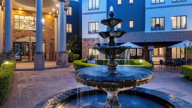 A courtyard with a central fountain, a building with multiple windows, and a well-maintained hedge. - Basdenwood Hotel  (Centurion)