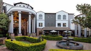 A courtyard with a fountain, manicured hedges, and a building with columns and a covered patio area. - Basdenwood Hotel  (Centurion)