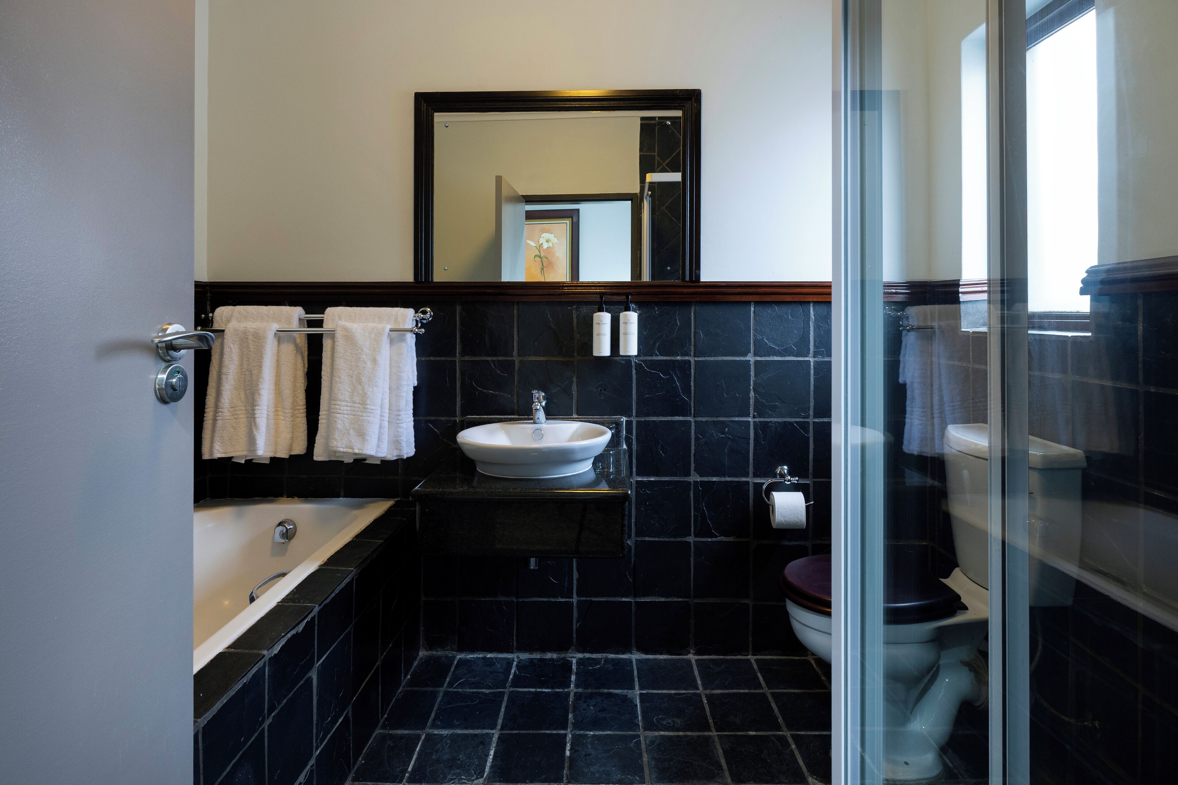 A bathroom with a bathtub, sink, and toilet, with black tiles and a mirror above the sink.