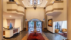 A grand lobby with a reception desk, a chandelier, a red carpet, and a view through a glass door. - Basdenwood Hotel  (Centurion)