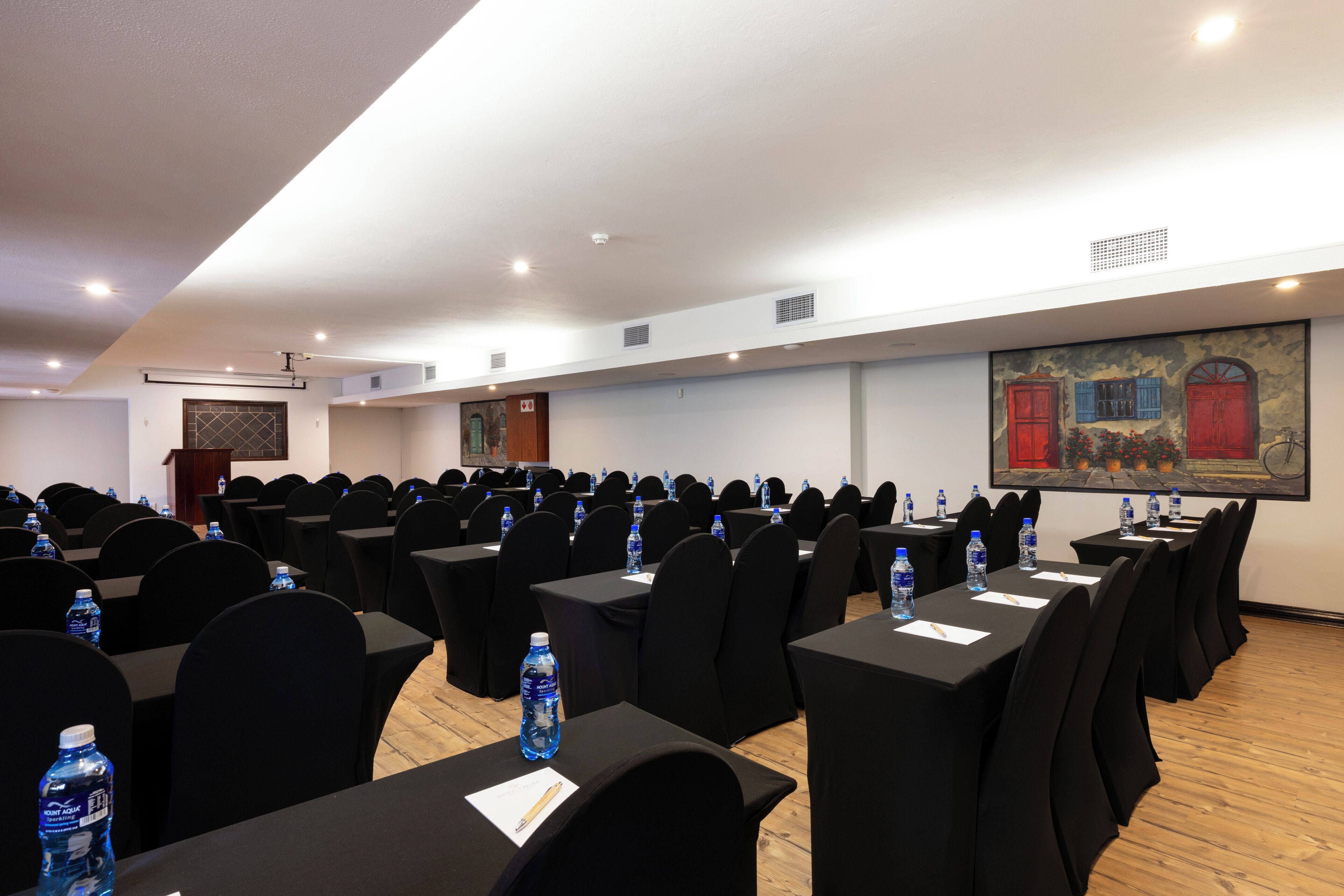 Une salle de conférence avec des rangées de tables, de chaises et des bouteilles d’eau.