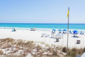A beach with white sand, clear blue water, and a flagpole with a yellow flag.