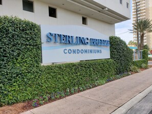A sign for Sterling Breeze Condominiums with a hedge and flowers in front.
