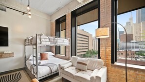Una habitación de hotel moderna con literas, un sofá, una lámpara y vistas a la ciudad.