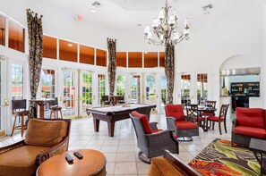 A pool table, lounge chairs, and a billiards table in a well-lit room with large windows and a chandelier. - Paradise Near the Parks at Solana (Davenport)