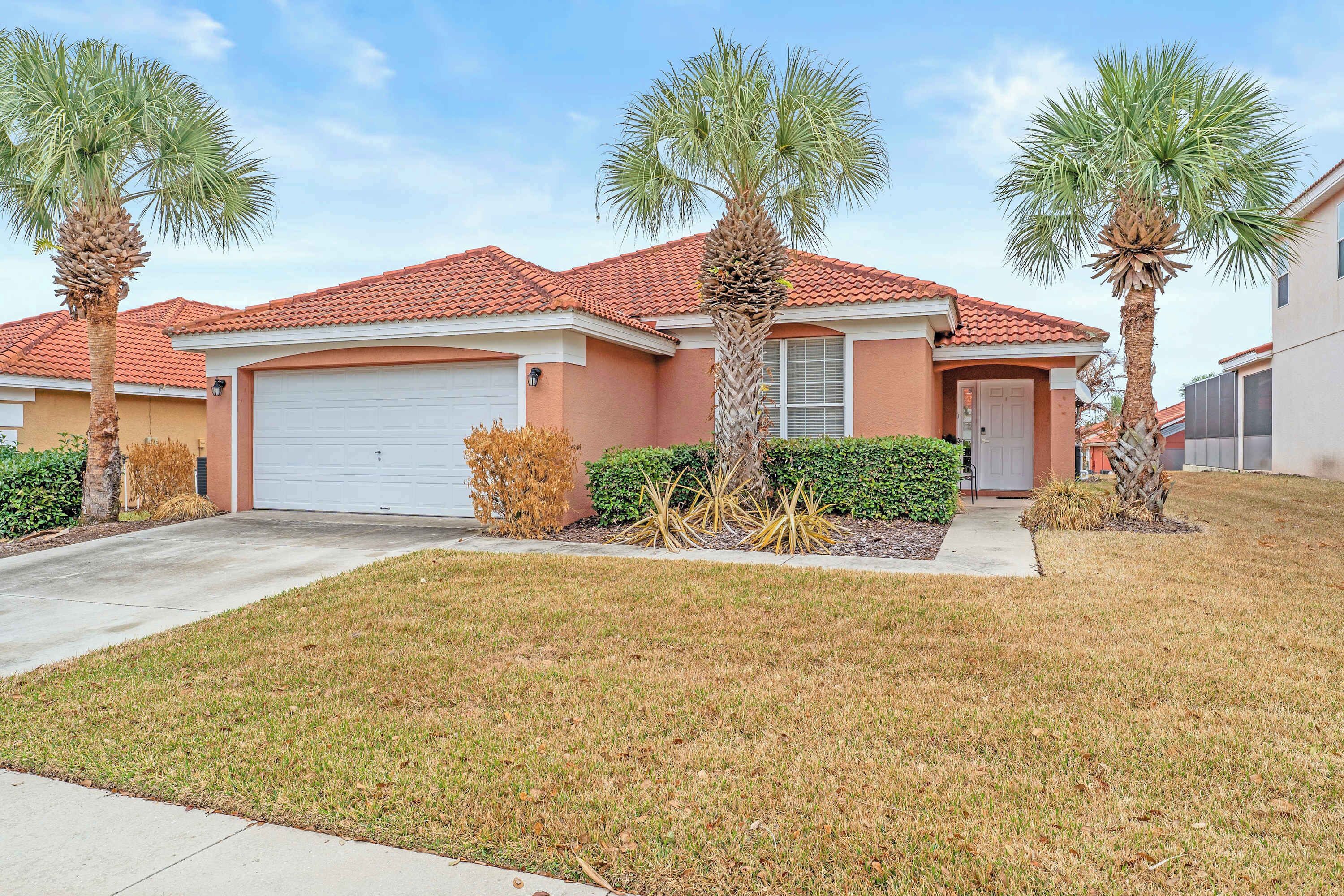 A residential house with a red-tiled roof, a garage, and a well-maintained lawn with palm trees.